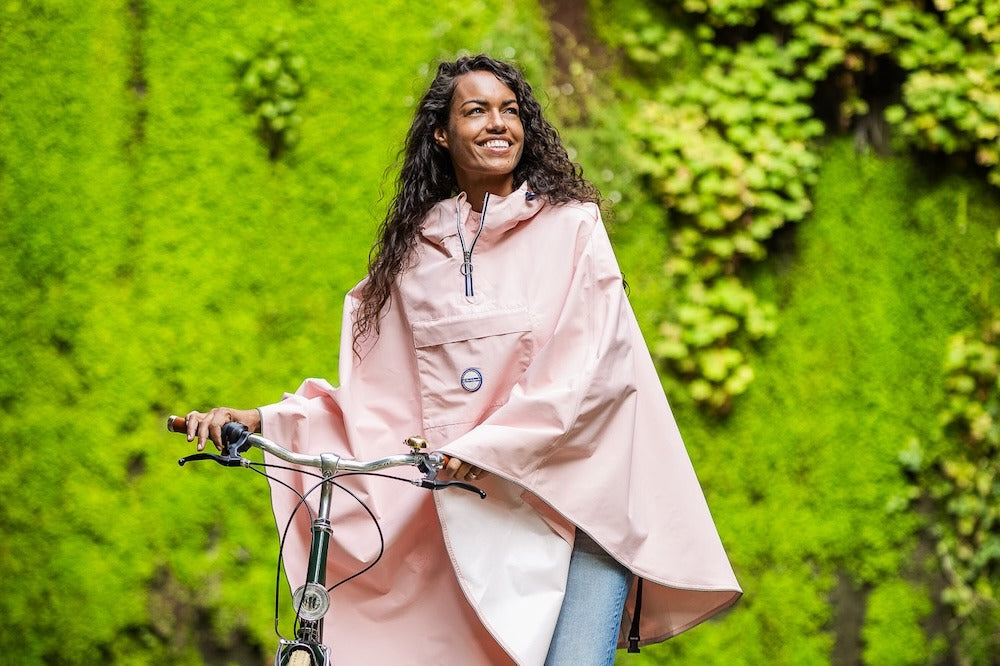 Cycliste souriante avec sa cape de pluie devant un mur végétal