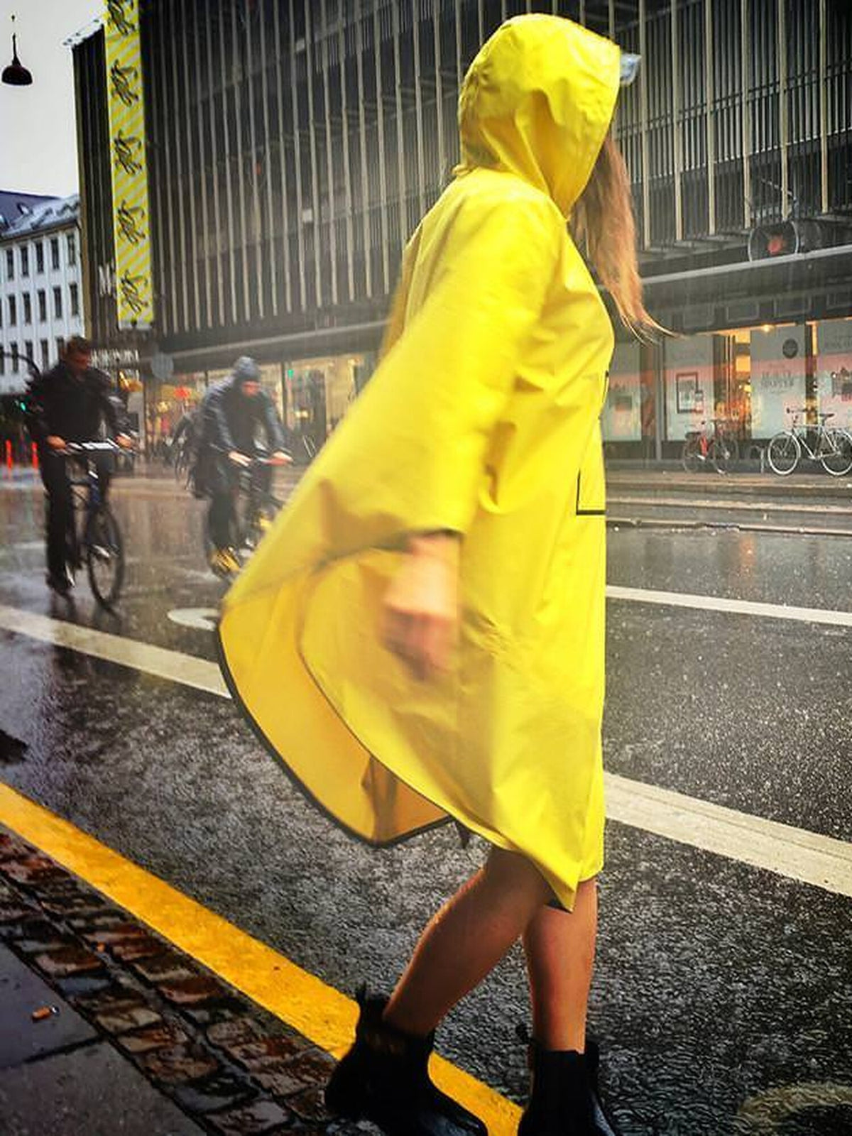 Poncho de pluie The People's Poncho jaune porté en ville sous la pluie, cyclistes en arrière-plan